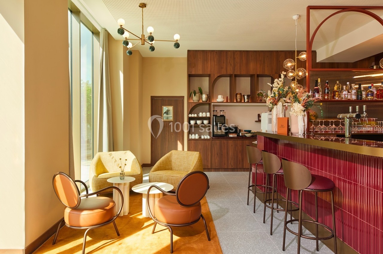 Espace lounge lumineux avec fauteuils, tables basses, bar en bois et étagères décoratives dans un décor moderne.
