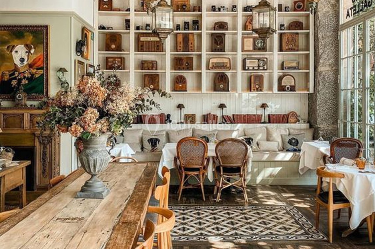 Salle lumineuse avec mobilier en bois, étagères décorées d'objets vintage, et tables dressées pour un repas.