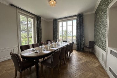 Salle de réunion lumineuse avec table en bois, chaises rembourrées, bouteilles d'eau et grandes fenêtres avec rideaux…