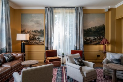 Salle de réunion lumineuse avec table en bois, chaises rembourrées, bouteilles d'eau et grandes fenêtres avec rideaux…