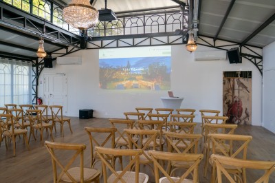 Salle de réunion lumineuse avec table en bois, chaises rembourrées, bouteilles d'eau et grandes fenêtres avec rideaux…