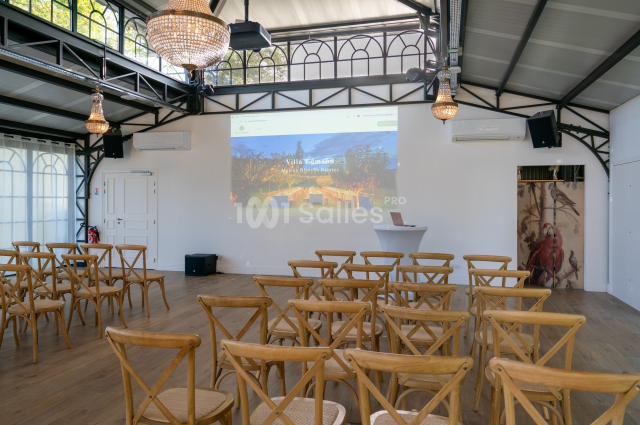 Salle lumineuse avec chaises en bois disposées face à un écran de projection dans un espace au style industriel.