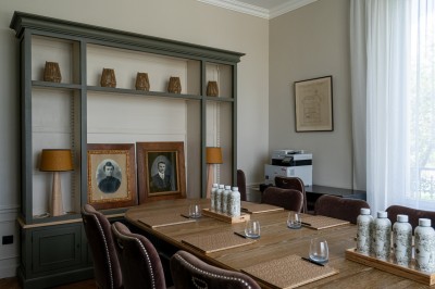 Salle de réunion lumineuse avec table en bois, chaises rembourrées, bouteilles d'eau et grandes fenêtres avec rideaux…