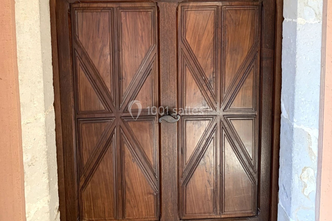 Porte en bois massif à deux battants avec motifs géométriques, encadrée de pierres claires.