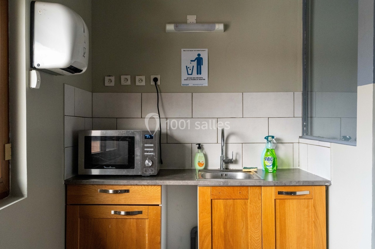 Coin cuisine avec micro-ondes, évier, produits ménagers et distributeur de papier mural, dans un espace sobre.