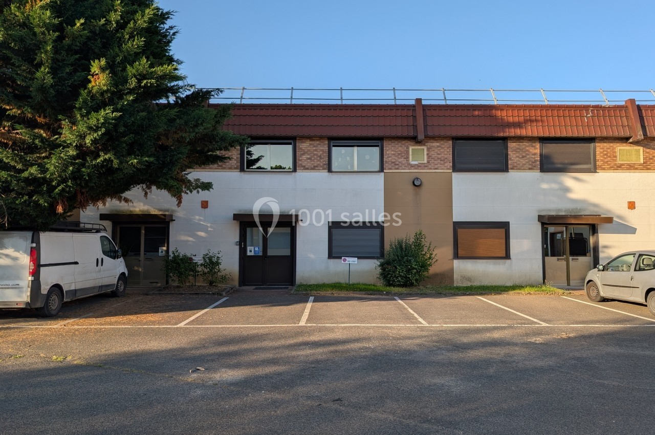 Façade d'un petit bâtiment commercial avec des places de parking et des véhicules stationnés à l'avant.