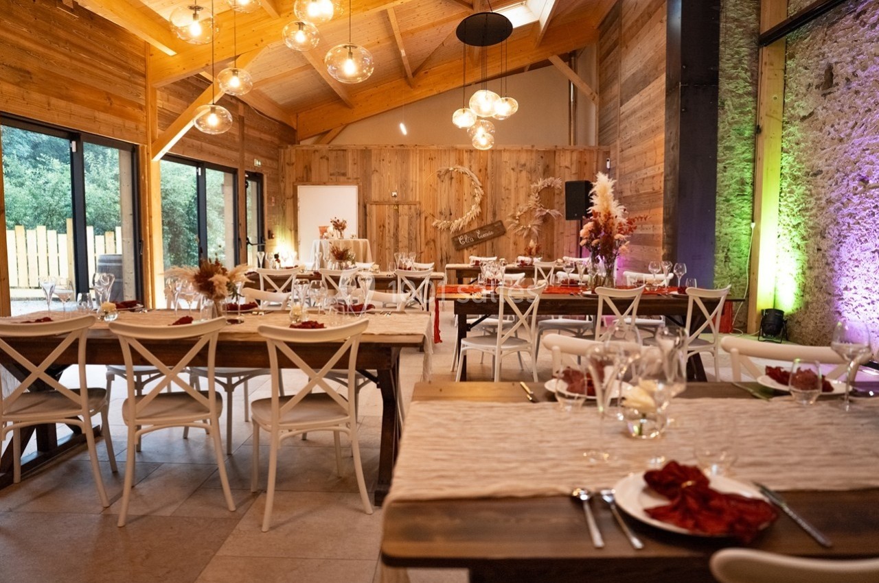 Salle de réception décorée avec des tables en bois, chaises blanches et éclairage chaleureux, ambiance rustique et élégante.