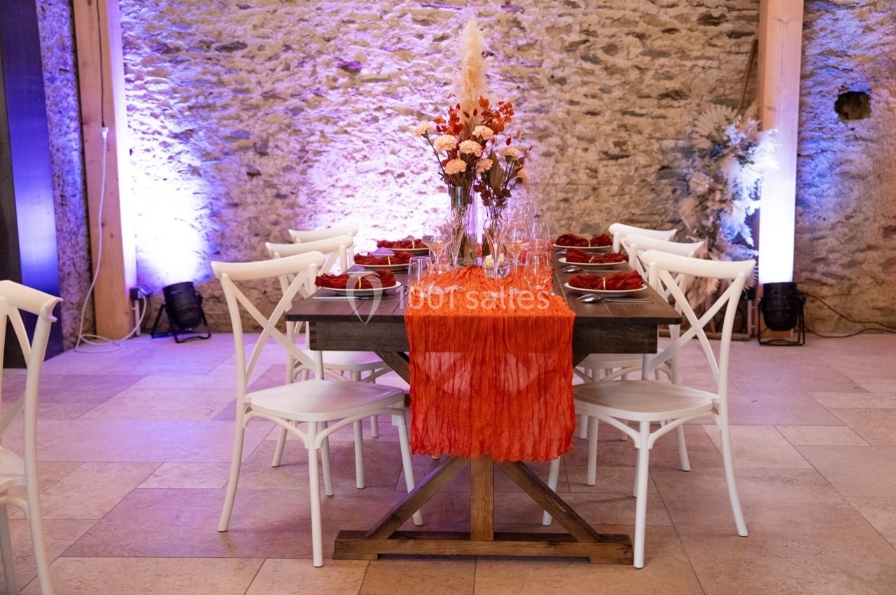Table décorée avec une nappe orange, des fleurs au centre, des assiettes rouges et des chaises blanches, dans une salle en…