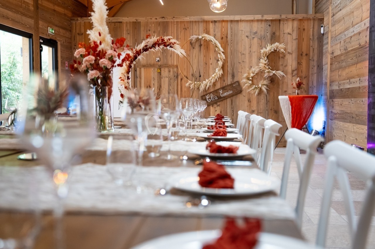 Salle de réception décorée avec des fleurs séchées, une longue table dressée et des serviettes rouges pliées.