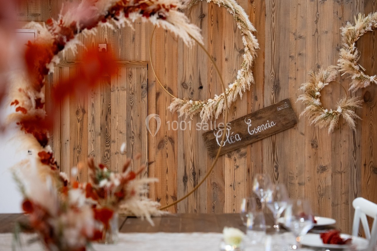 Décoration de mariage avec des couronnes de fleurs séchées, un panneau en bois et une table dressée au premier plan.