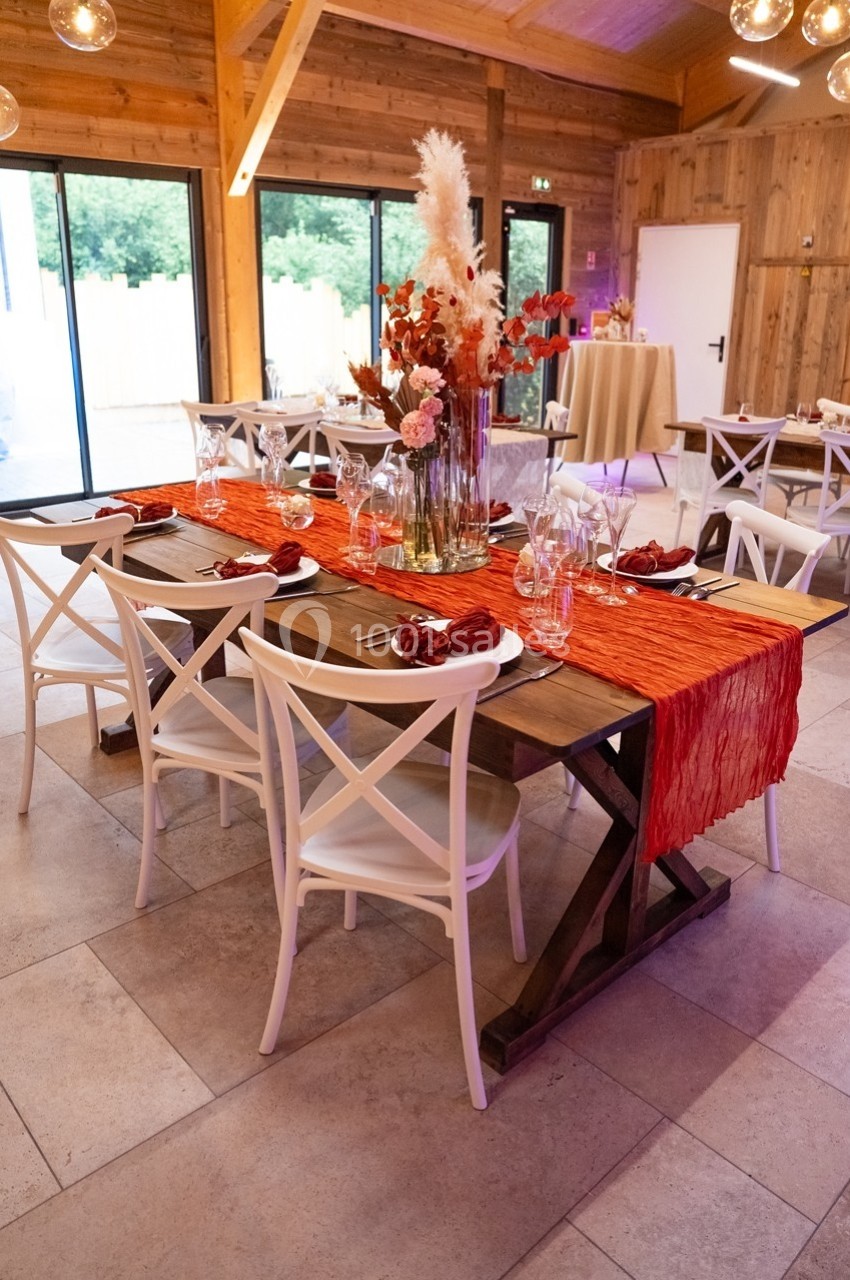 Table en bois décorée avec un chemin de table rouge, des fleurs et de la vaisselle, dans une salle au style rustique.
