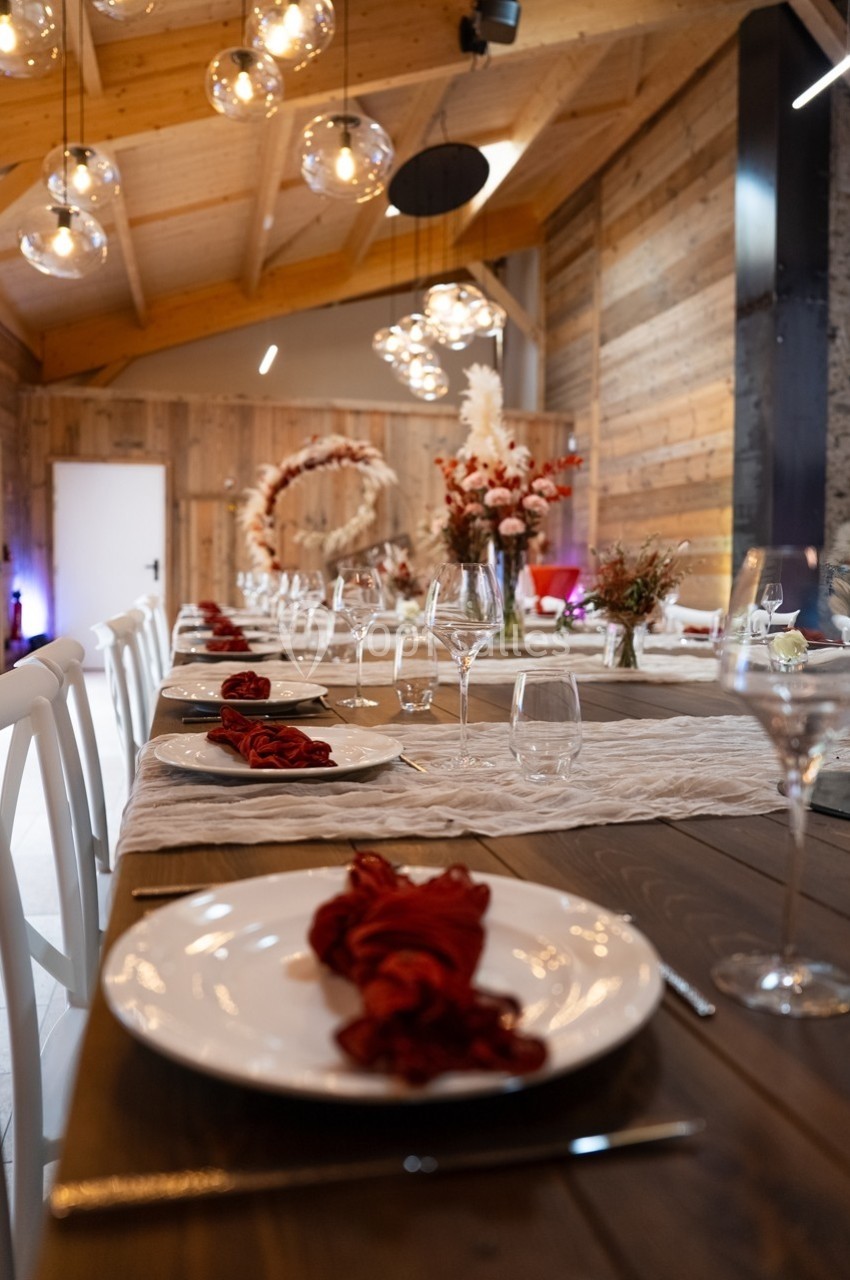 Table en bois dressée avec des assiettes blanches, serviettes rouges et verres, dans une salle au décor chaleureux en bois.