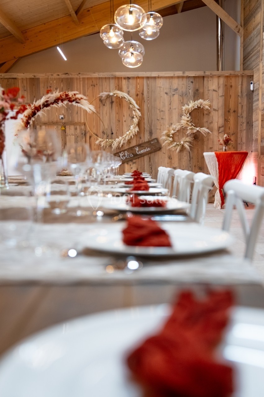 Salle de réception décorée avec des tables dressées, des serviettes rouges et des éléments en bois et fleurs séchées.