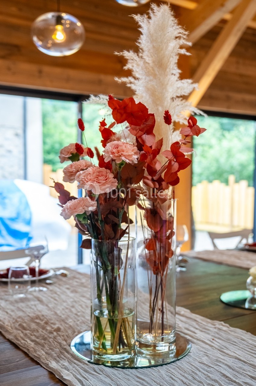 Bouquet de fleurs séchées et fraîches dans des vases en verre, posé sur une table en bois dans un intérieur lumineux.