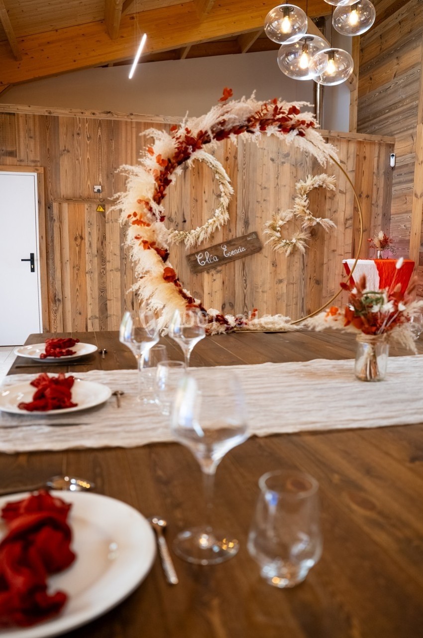 Décoration de table avec serviettes rouges, centre de table floral et arche ornée de pampas et feuilles rouges en arrière…