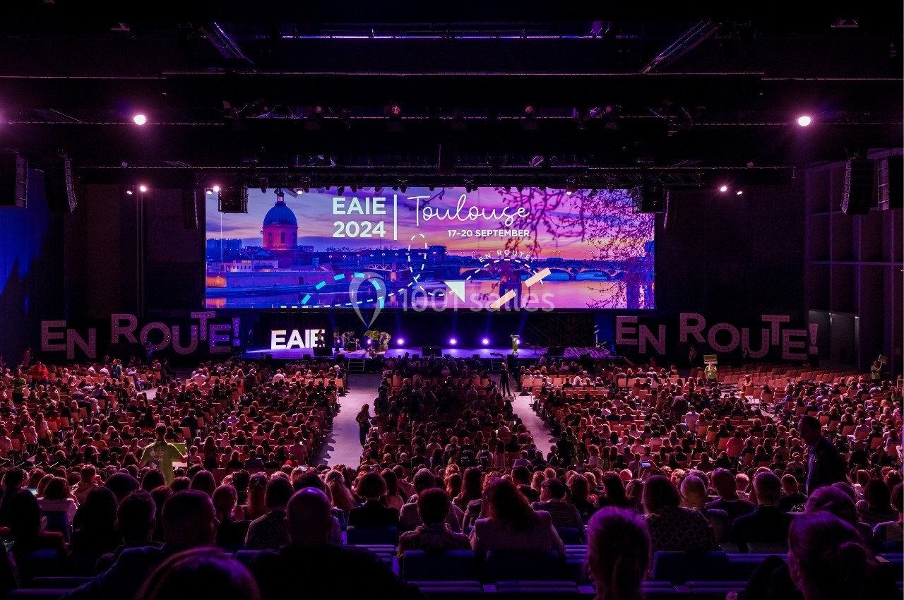 Salle de conférence bondée avec une scène illuminée affichant ’EAIE 2024 Toulouse 17-20 septembre’.