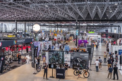 Vue d'un salon professionnel avec des stands exposant des vélos et des accessoires dans un grand hall lumineux.