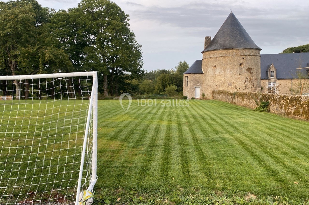 But de football sur une pelouse bien entretenue, avec un bâtiment en pierre et une tour en arrière-plan.