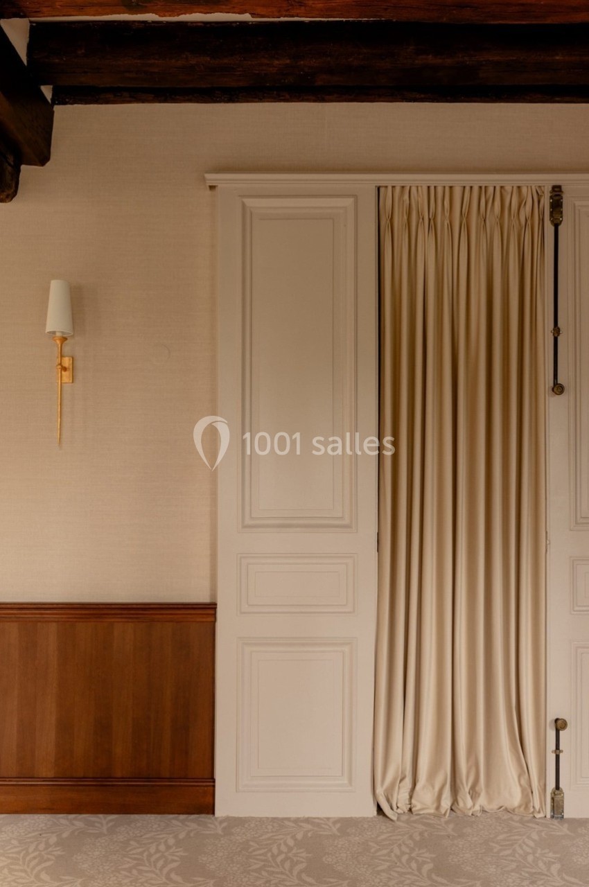 Porte blanche avec rideaux beiges fermés, mur en bois et applique murale dorée sur fond de papier peint clair.