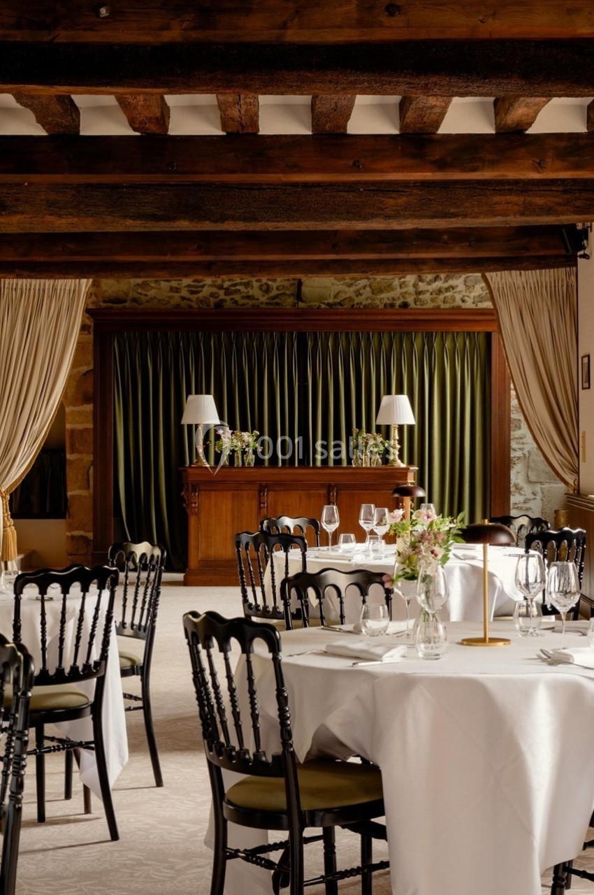 Salle de réception élégante avec tables rondes dressées, chaises noires et rideaux verts encadrant un buffet en bois.