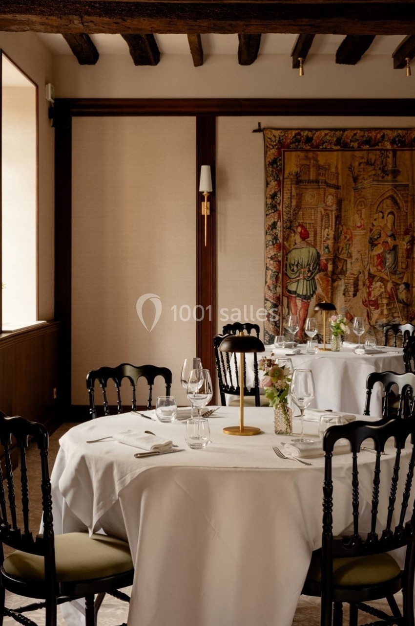 Salle de restaurant élégante avec tables dressées, nappes blanches, chaises noires et tapisserie murale décorative.