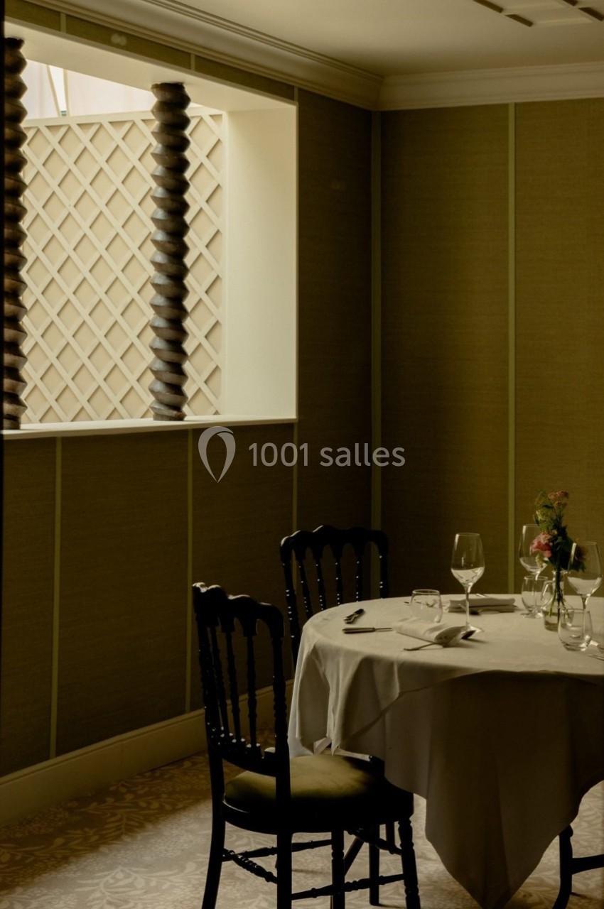 Salle de restaurant élégante avec une table dressée pour deux, éclairée par une lumière douce près d'une fenêtre.