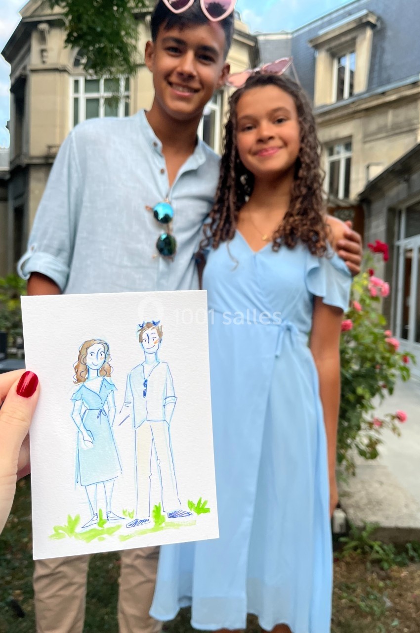 Une personne tient un dessin représentant deux jeunes posant devant un bâtiment ancien avec des roses en arrière-plan.
