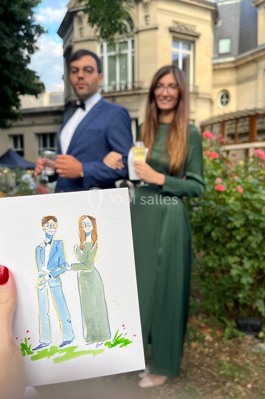 Un couple élégant pose dans un jardin, tenant des boissons, avec un dessin les représentant au premier plan.