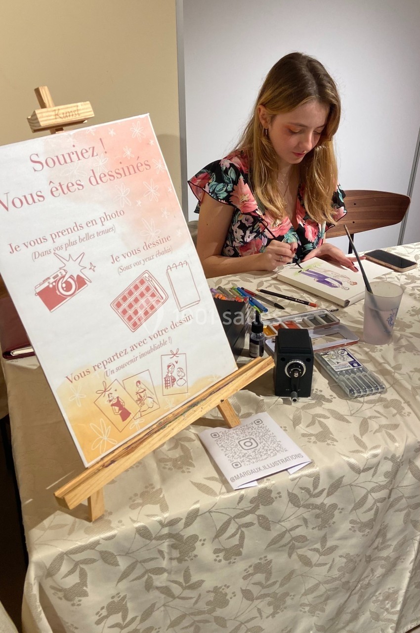 Une artiste peint une personne à une table, avec un chevalet affichant des instructions pour obtenir un dessin personnalisé.