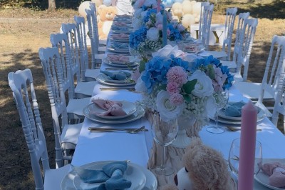 Table élégamment dressée avec nappes blanches, vaisselle raffinée, bougies roses et décoration florale assortie.