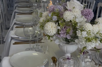 Table élégamment dressée avec nappes blanches, vaisselle raffinée, bougies roses et décoration florale assortie.