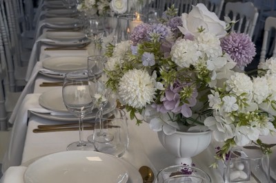 Table élégamment dressée avec nappes blanches, vaisselle raffinée, bougies roses et décoration florale assortie.