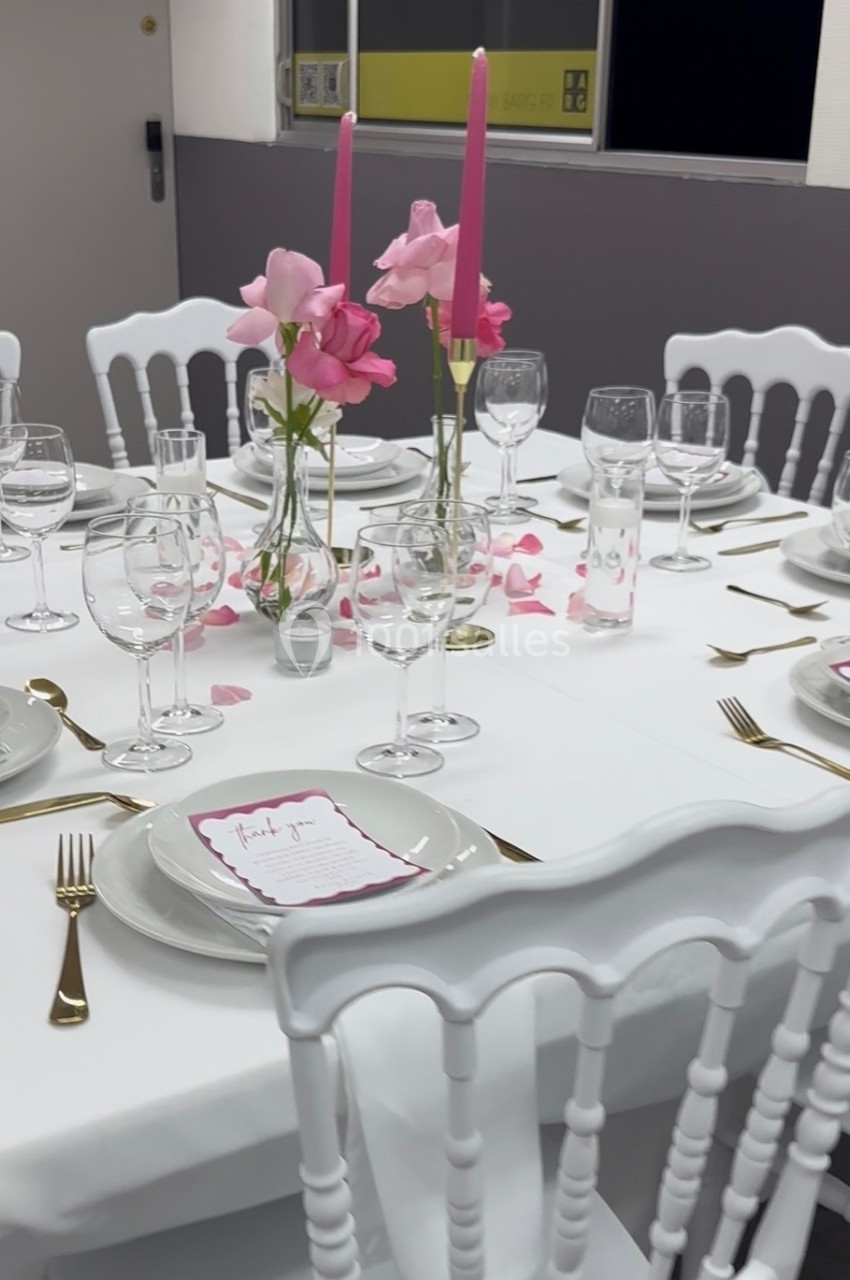 Table élégamment dressée avec nappes blanches, vaisselle raffinée, bougies roses et décoration florale assortie.