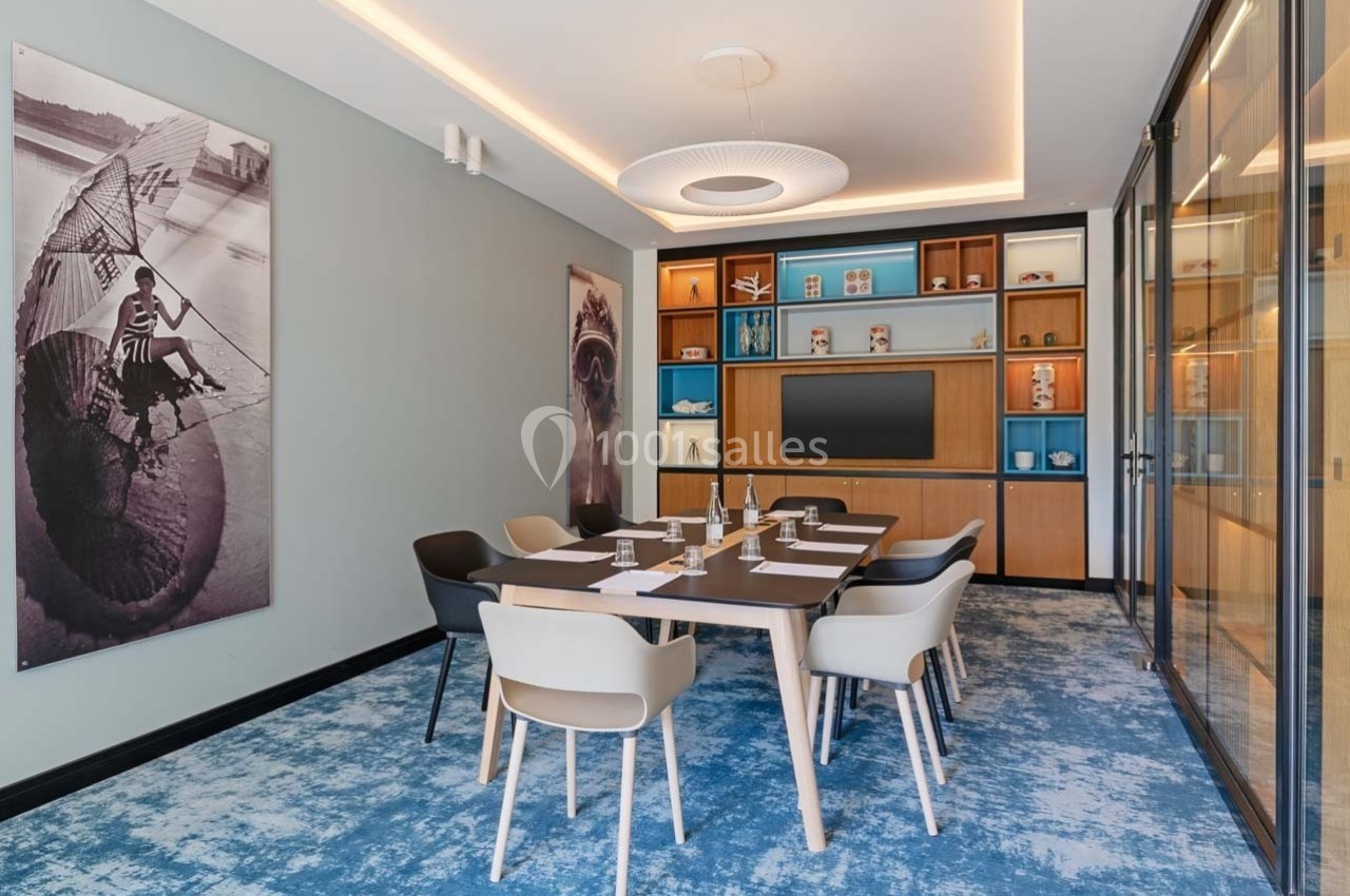 Salle de réunion moderne avec table, chaises, écran mural, étagères décoratives et éclairage intégré.