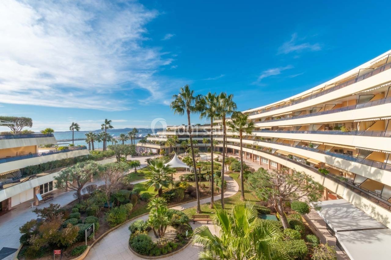 Vue d'une cour intérieure arborée entourée de bâtiments modernes en bord de mer sous un ciel bleu.