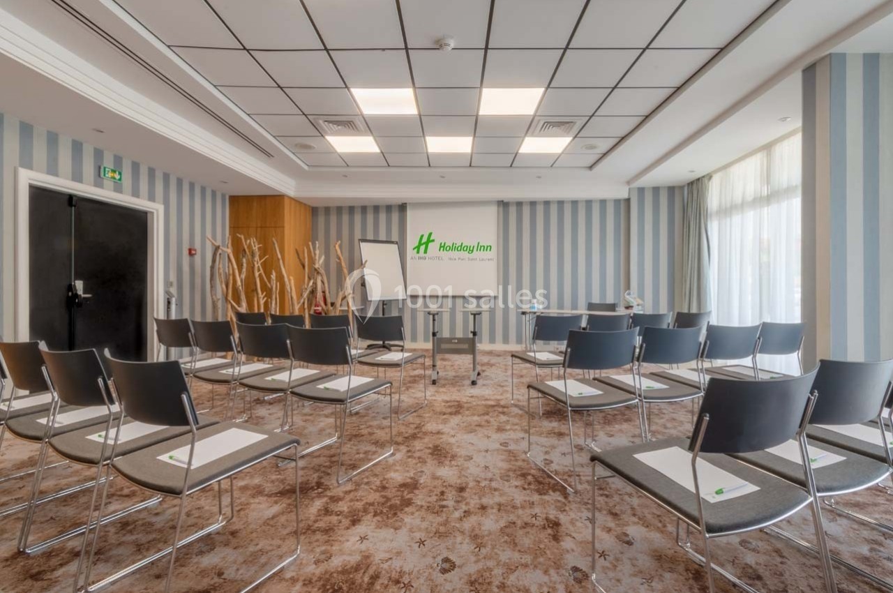 Salle de réunion lumineuse avec chaises disposées en rangées, tableau blanc et logo Holiday Inn sur le mur.