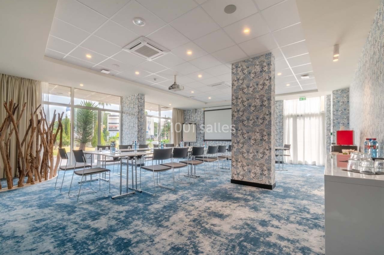 Salle de réunion lumineuse avec chaises, tables, projecteur, grandes baies vitrées et décorations modernes.