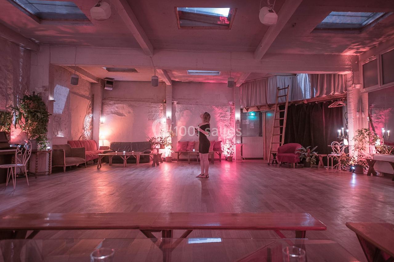 Une femme debout seule dans une grande salle éclairée par des lumières tamisées roses et entourée de meubles.