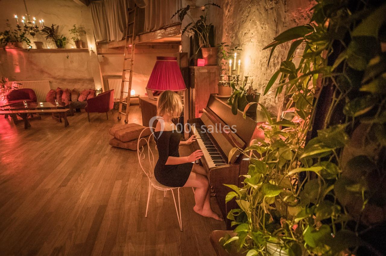 Une femme joue du piano dans une pièce chaleureusement éclairée, entourée de plantes et de meubles en bois.