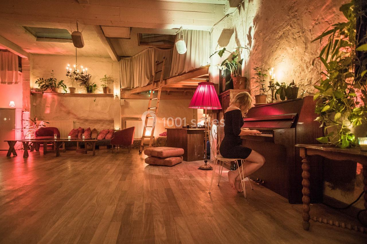 Une femme joue du piano dans une pièce chaleureuse éclairée par des lampes et décorée de plantes et de coussins.