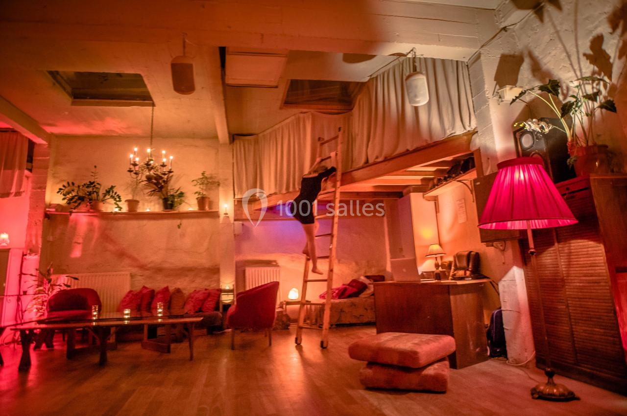 Espace intérieur chaleureux avec éclairage tamisé, mobilier en bois, plantes et mezzanine accessible par une échelle.