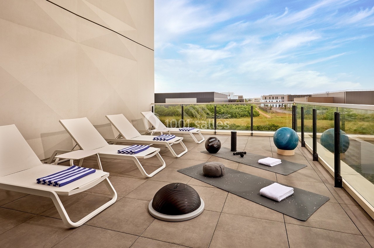 Terrasse avec chaises longues, tapis de sport, accessoires de fitness et vue sur un paysage dégagé.