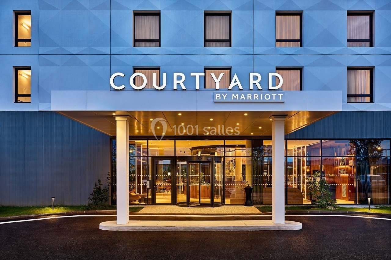 Façade d'un hôtel moderne avec enseigne ’Courtyard by Marriott’, entrée vitrée et éclairage chaleureux.