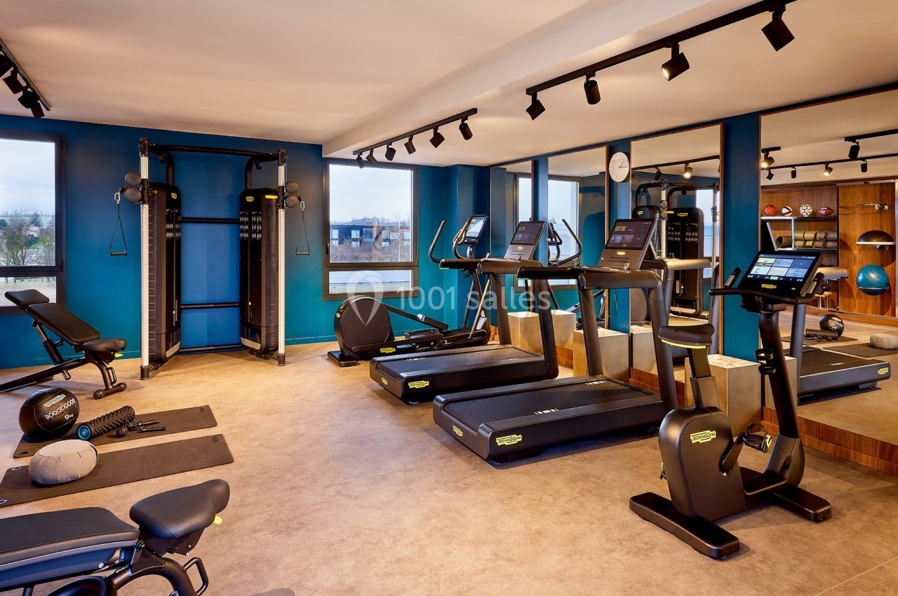 Salle de sport moderne avec tapis de course, machines de musculation et équipements divers dans un espace lumineux.