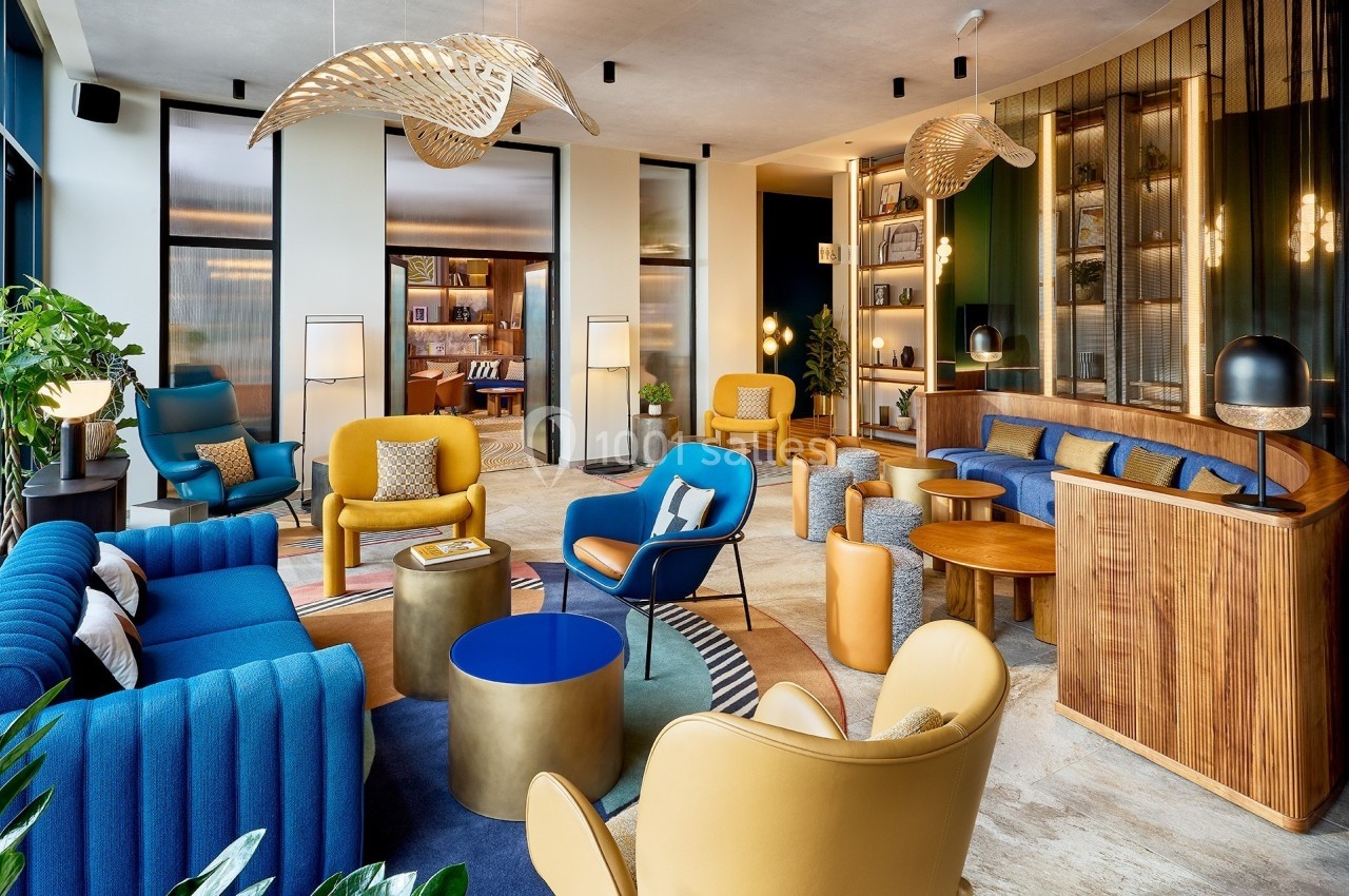 Salon moderne avec mobilier coloré, éclairage design, étagères décorées et grandes fenêtres laissant entrer la lumière…