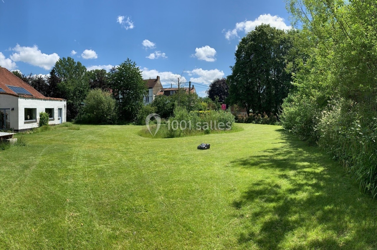 Jardin spacieux avec pelouse, arbres et maison en arrière-plan sous un ciel bleu parsemé de nuages.