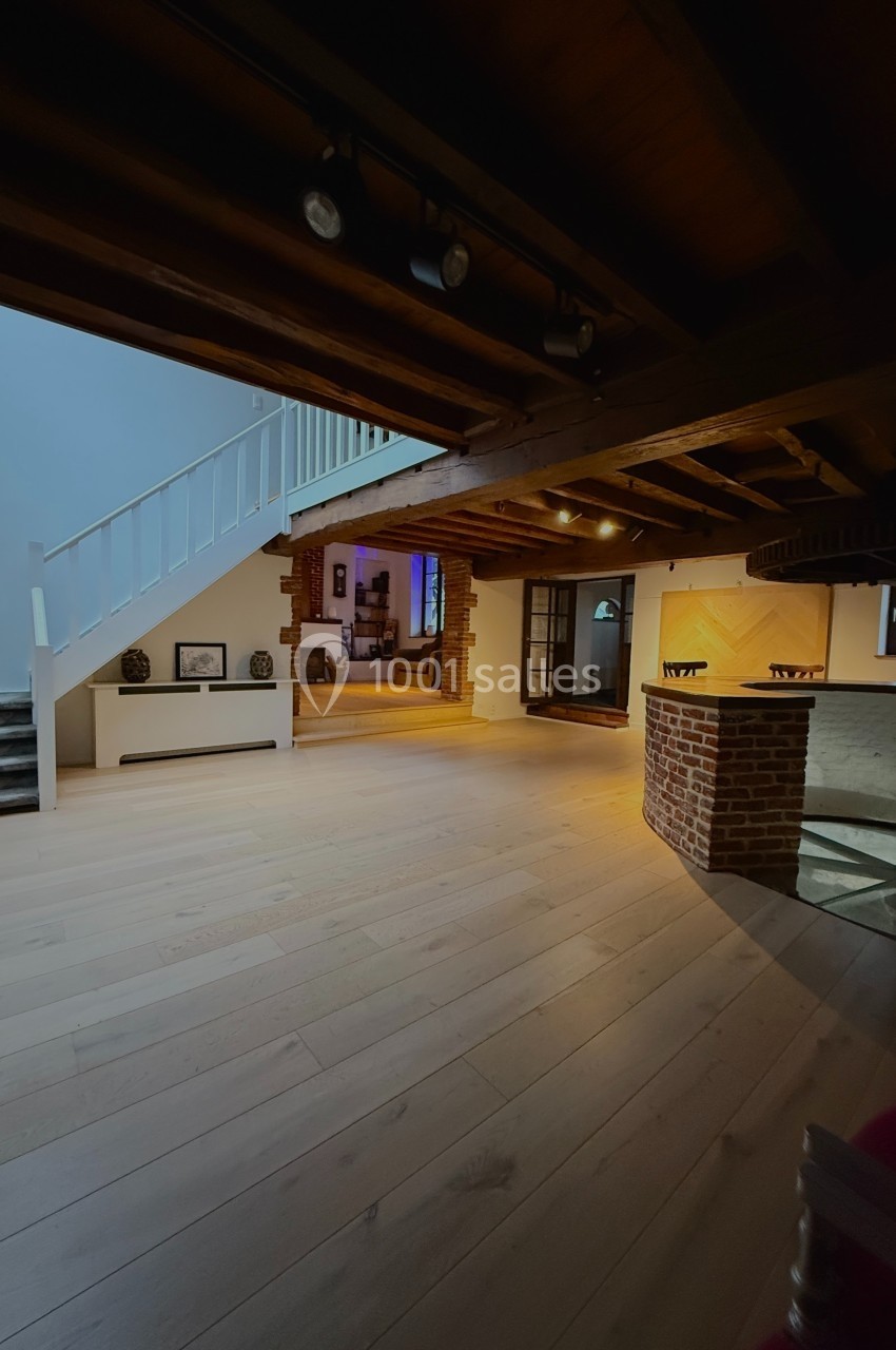Intérieur d'une maison avec escalier blanc, poutres apparentes, parquet clair et un bar en briques.