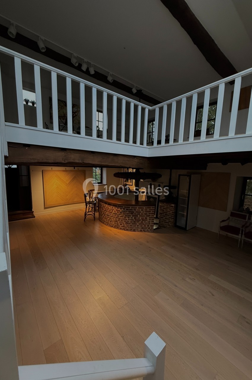 Vue d'un intérieur avec un espace ouvert, un bar en briques, un parquet clair et une mezzanine avec rambarde blanche.