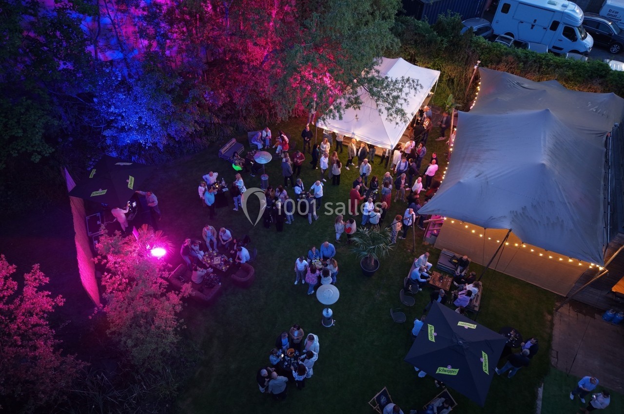 Vue aérienne d'une fête en plein air avec des tentes éclairées, des invités rassemblés et des lumières colorées.
