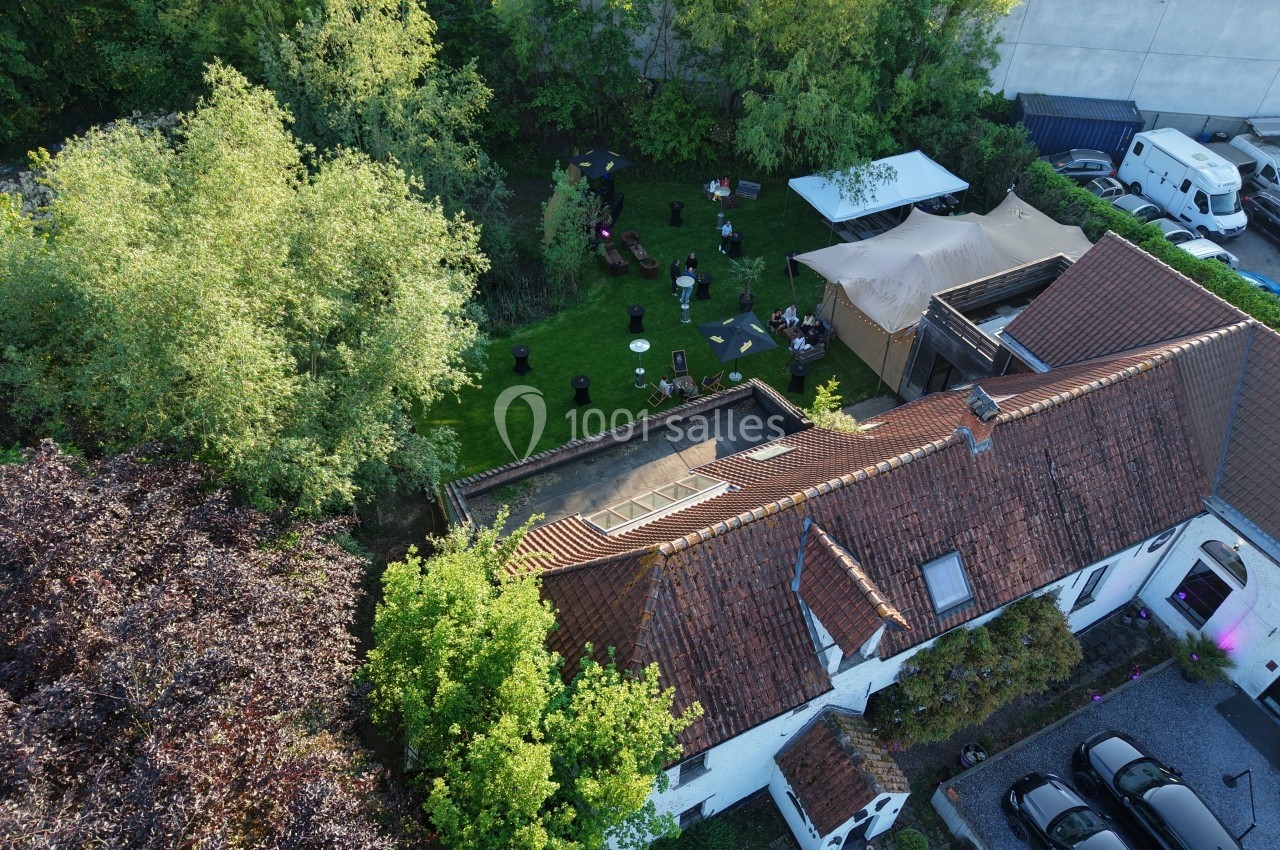 Vue aérienne d'une maison avec un jardin aménagé, des tables, des chaises et des arbres environnants.